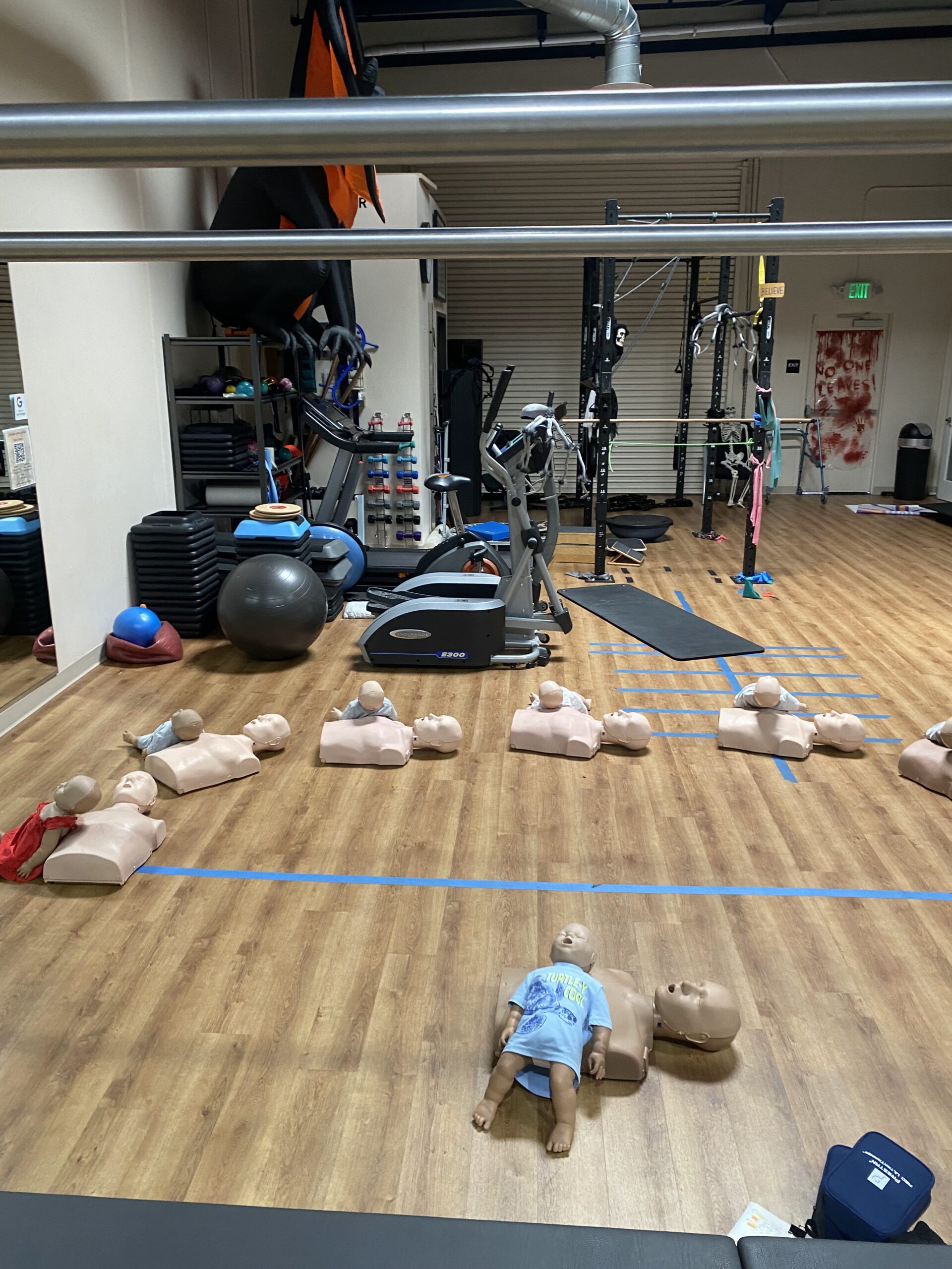Baby dolls lined up on a wooden floor in a gym with exercise equipment.